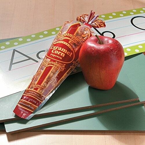 Caramel corn in a cone-shaped bag and a red apple on a desk with school supplies.